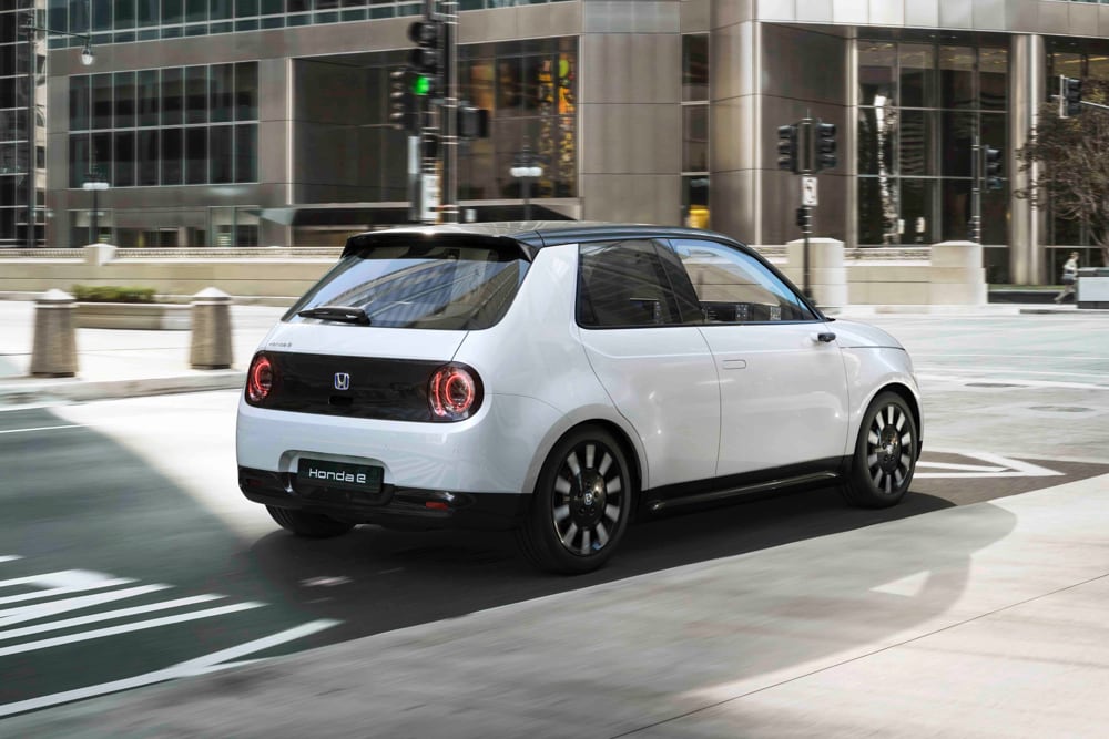 Rear shot of White Honda e driving down a city street.