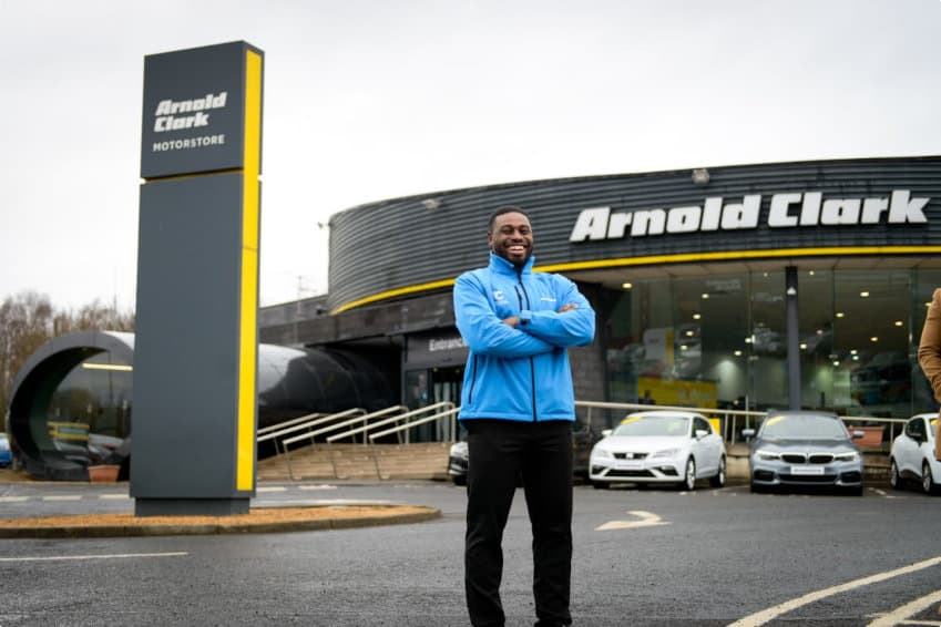 Product Genius standing in front of an Arnold Clark dealership with arms folded and smiling